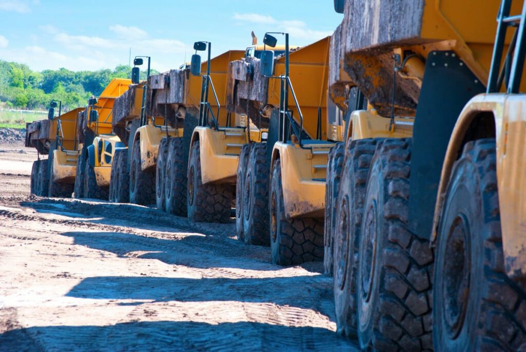 Image of a line of large yellow trucks leaving a muddy site, close up